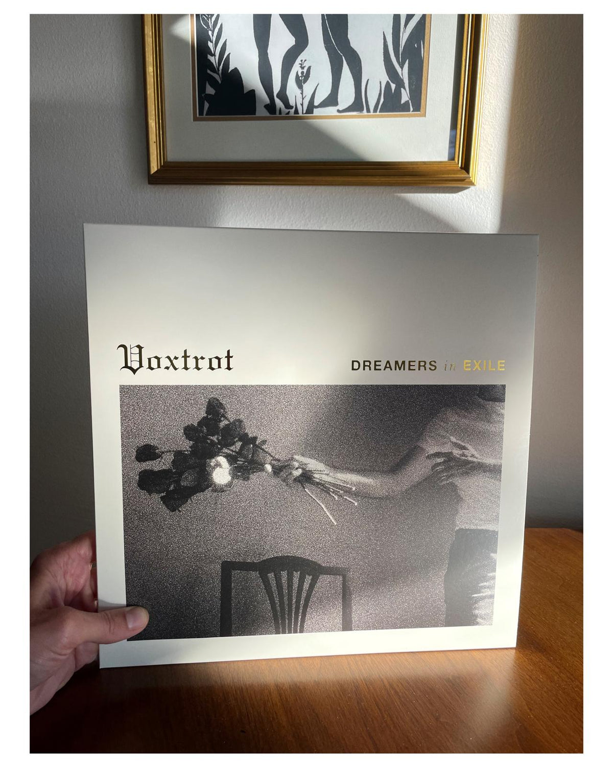 Album cover held by a hand with 'Voxtrot' and 'Dreamers in Exile' text on a gray background.